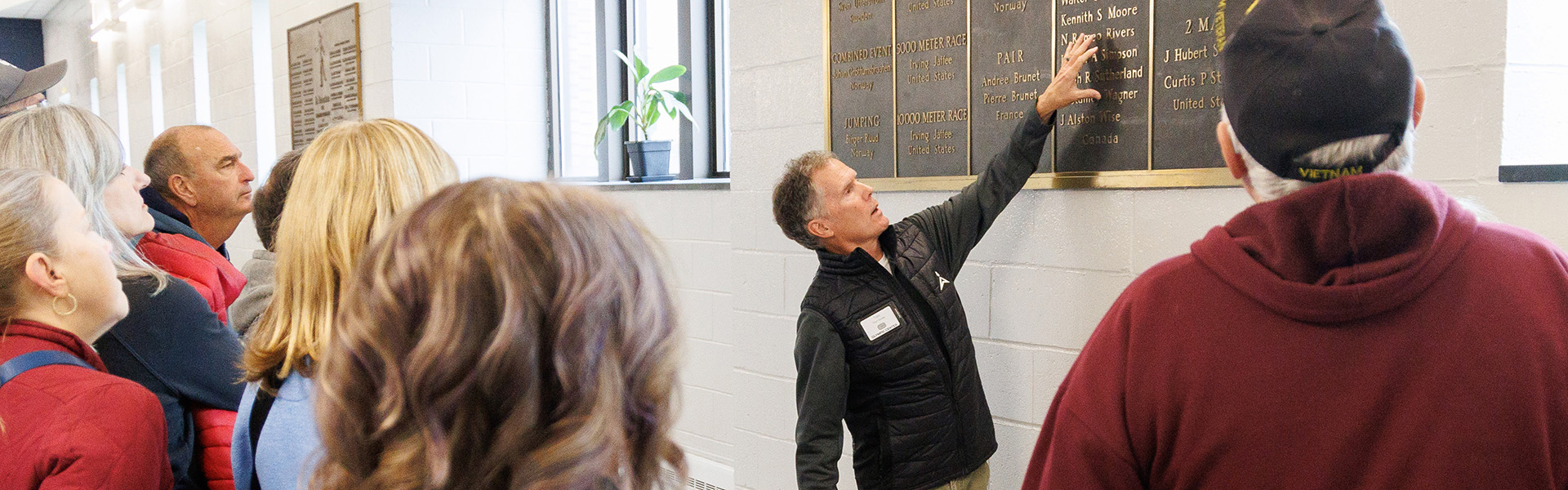 A man points at a plaque and describes it's contents to onlookers